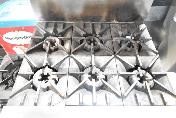 Garland SunFire stainless steel commercial 6-burner gas range with oven, overshelf, and backsplash; signs of use visible.