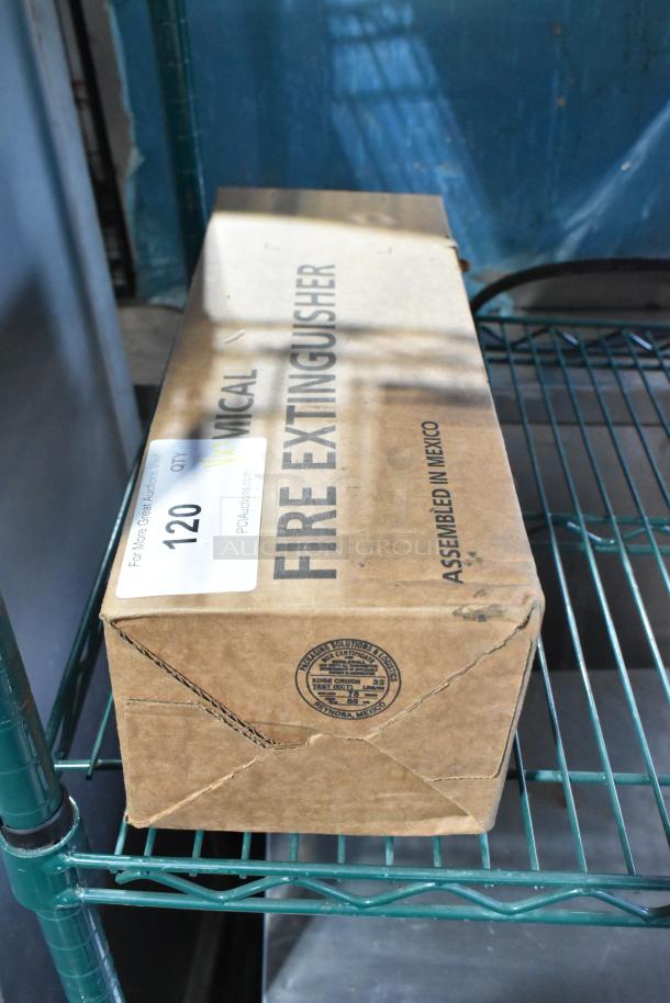 Cardboard box labeled "Fire Extinguisher" on a metal shelf. Shipping label states auction lot number 120. Box shows minor dents.