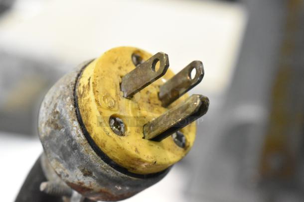 Close-up of a yellow plug from a Butcher Boy B12-F meat saw, showing wear, three metal prongs, 115 volts, 1 phase.