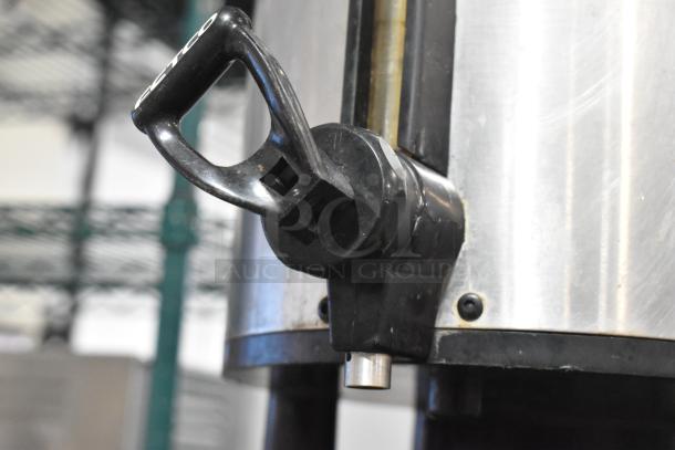 Fetco Luxus stainless steel beverage dispenser, used, with durable black spout and handle, featuring Fetco branding.