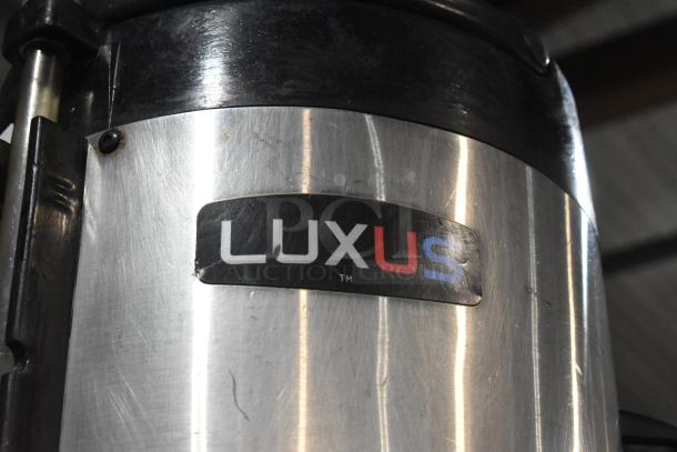 Fetco Luxus stainless steel beverage holder, commercial countertop dispenser, features Luxus branding, minor wear visible.