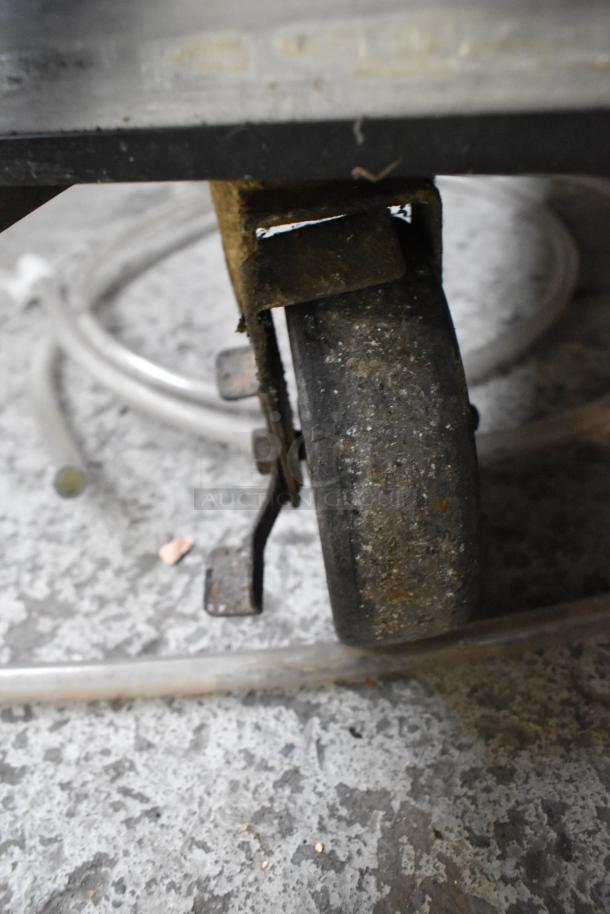 Close-up of a commercial caster on a True TUC-48 undercounter cooler, showing signs of wear on a textured floor surface.