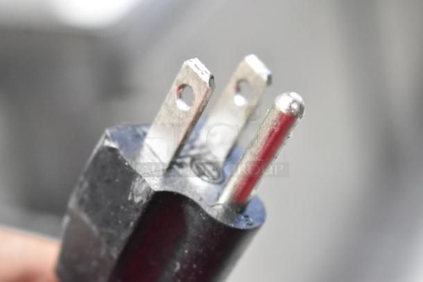 Close-up of a three-prong electrical plug for the Winco FW-L600 food warmer. Black casing with metallic prongs.