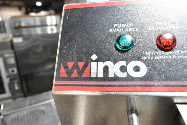 Winco stainless steel countertop electric deep fat fryer with metal fry basket, 115 volts, single phase, lights indicating power and heat.