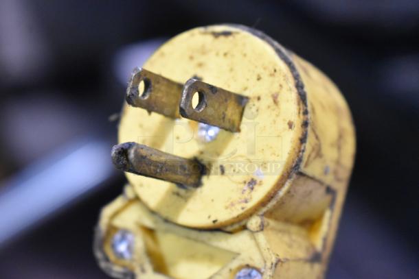 Yellow electrical plug with three prongs, showing signs of wear and dirt accumulation.