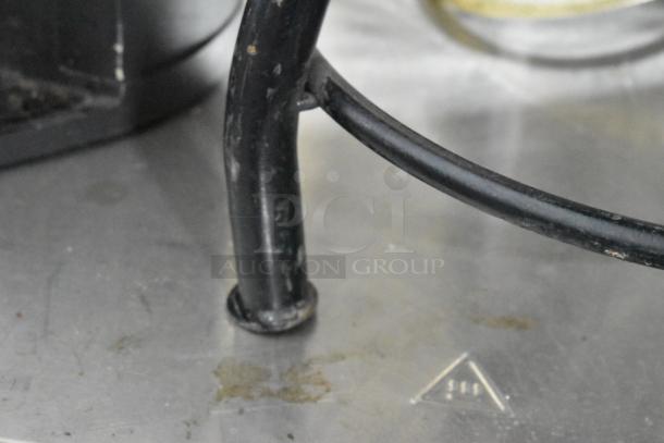 Close-up of a black metal stool leg on a wooden floor, showing signs of wear and surface marks.
