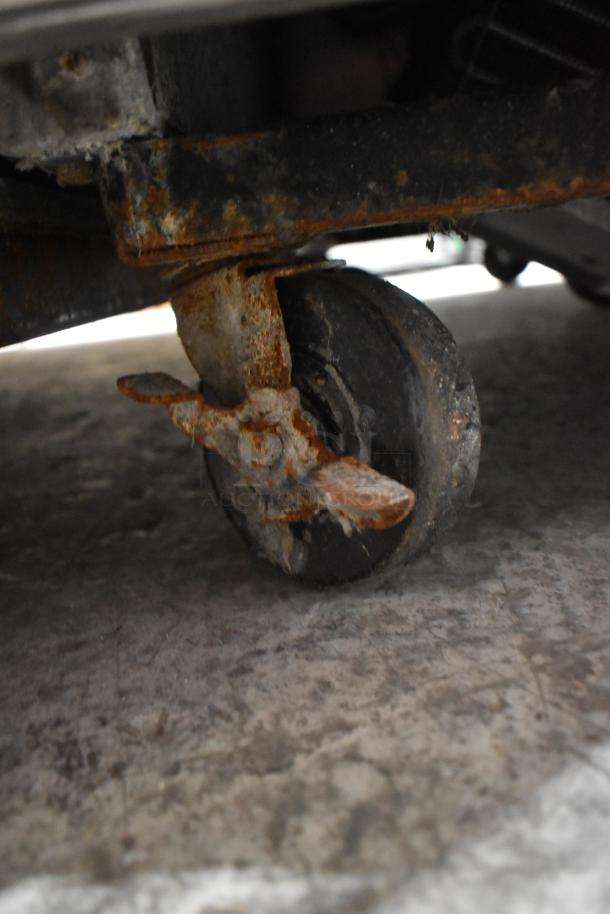 Close-up of a rusted caster on a True T-23F stainless steel commercial freezer. Signs of wear visible.