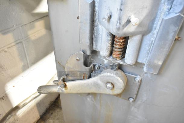 Metal commercial floor-style meat saw close-up, showcasing lever and spring mechanism. Features visible wear, indicating use.