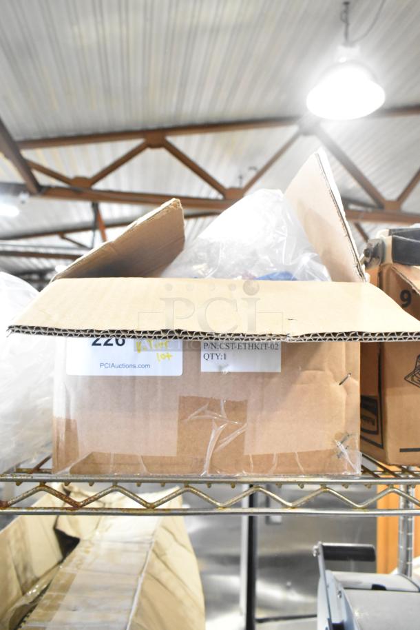 Cardboard box labeled "PCI Auctions" on a metal shelf, containing Rubbermaid amber drop-in bins, cables, and brackets.