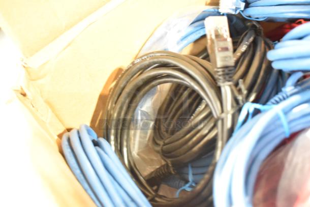 Box of assorted cables, including coiled black cables and blue Ethernet cords. Suitable for electronics use.