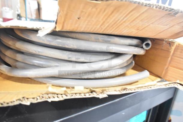 Coiled Global Manufacturing EF-INTERLOCK Hose in cardboard box, gray, appears lightly used. Suitable for industrial applications.