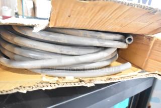 Coiled Global Manufacturing EF-INTERLOCK Hose in cardboard box, gray, appears lightly used. Suitable for industrial applications.