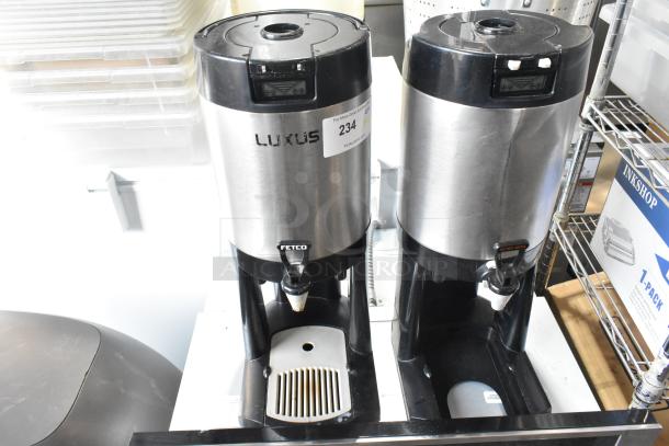 Two stainless steel Fetco countertop beverage dispensers with black lids and bases, in used condition.