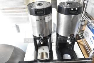 Two stainless steel Fetco countertop beverage dispensers with black lids and bases, in used condition.