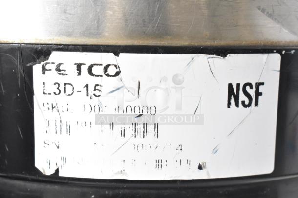 Metal beverage holder dispenser with label reading "Fetco L3D-15" and "NSF" marking, showing visible wear.