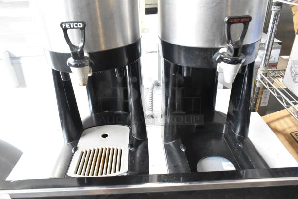 Two Fetco metal countertop beverage dispensers, black base, visible spouts, functional condition.