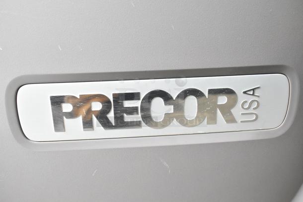 Precor Floor Style Elliptical logo close-up. Silver Precor USA emblem on gray background. Ideal for home gyms. 120V, 1 Phase.