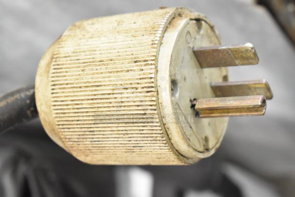 Close-up of a worn plug for an Alto Shaam 1000-TH commercial oven, showing three metal prongs and ribbed grip.