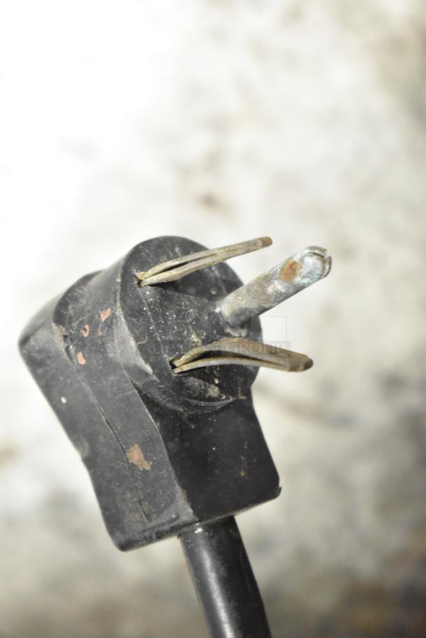 Close-up of a metal commercial bottle vending machine's power plug, showing three prongs with visible wear. 115 volts, 1 phase.