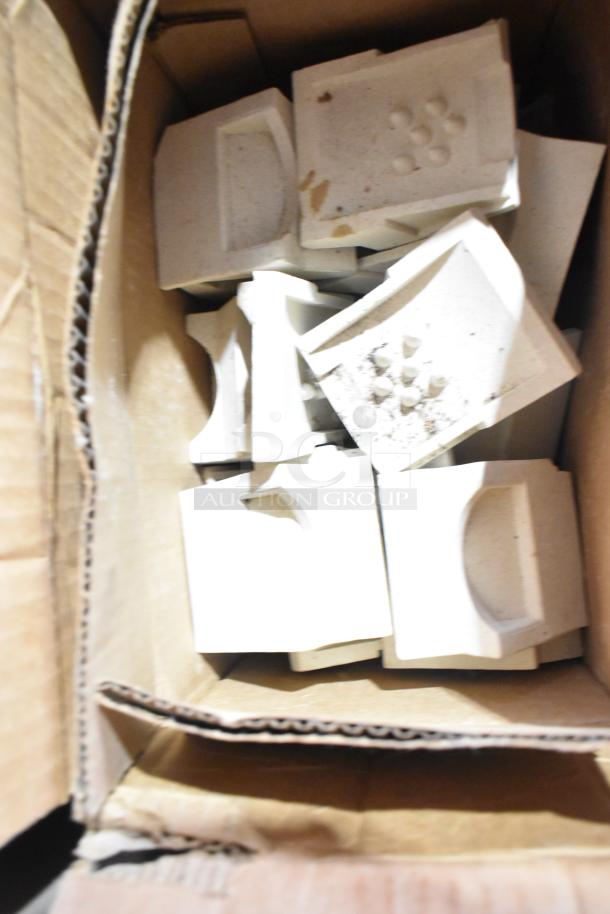 Cardboard box containing various white ceramic molds with textured surfaces, part of auction tier lot.