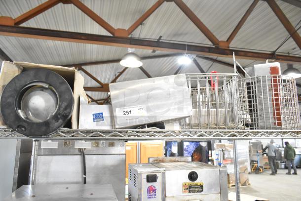 Auction lot of various items on a metal shelf, including a black plastic cup dispenser, metallic fry basket, and assorted metal pieces. Item tag 251 visible.