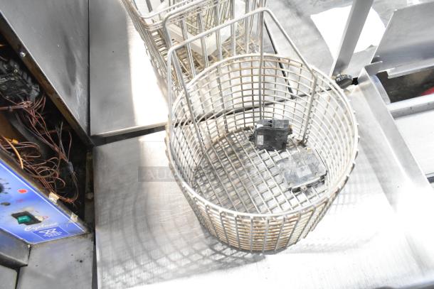 Lot of various items including a metal fry basket, cup dispenser, and metal pieces on a stainless steel surface.