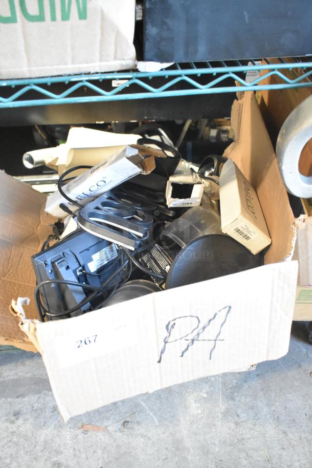 Lot of assorted items in a cardboard box, including a telephone, open sign, cameras, and speakers; mixed condition.