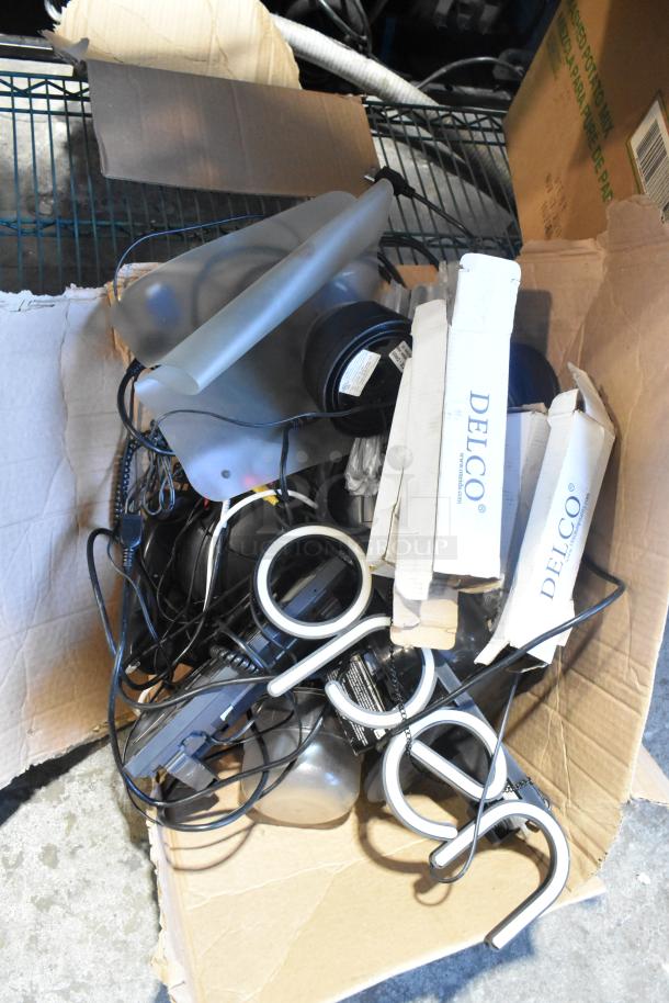 Box of assorted electronic items, including telephones, open sign parts, cameras, speakers, and DELCO packaging. Mixed condition.