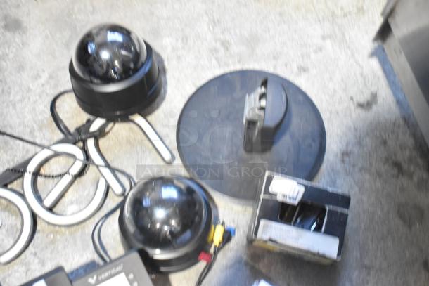 Lot of various items including dome cameras, a black circular open sign, and electronic cables on a gray surface.