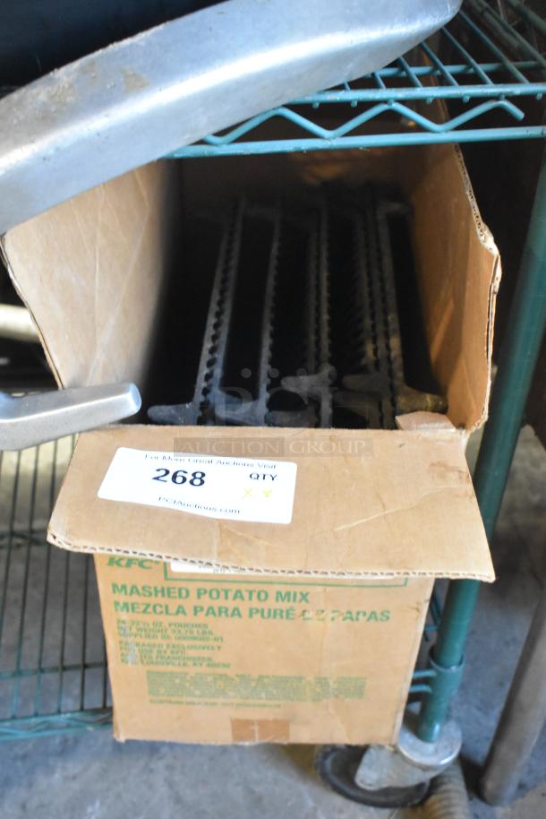 Cardboard box containing 8 metal grates with serrated edges, labeled "268." Grates appear unused, placed on a metal shelf.