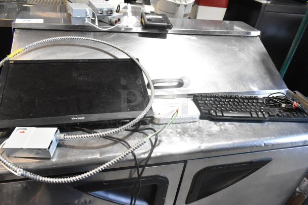 Metal cash drawer, ViewSonic monitor, keyboard, and cables on stainless steel surface. Various cords and devices included.