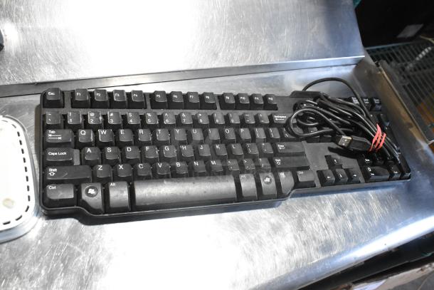 Black wired keyboard with USB connector, slightly worn keys, shown on a metallic surface. Part of a 10-item auction lot.