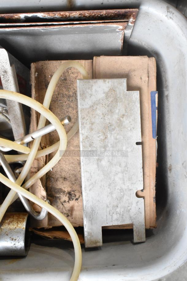 Bin with assorted metal pieces, tubing, and cardboard. Items are old and worn, suggesting potential for repurposing.