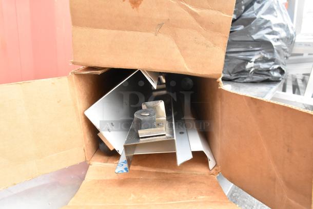 Stainless steel equipment stand with metal under shelf, viewed in a partially open cardboard box, showing pristine condition and assembly parts.