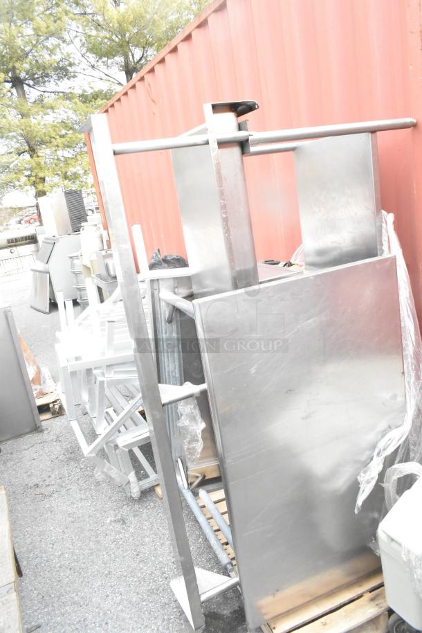 Three stainless steel tables with sturdy frames, varying sizes, outdoor setting, minor wear, located near a storage unit.