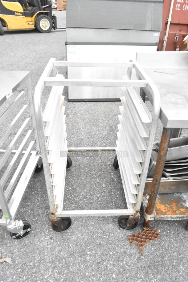 Metal bun/sheet pan rack on commercial casters, holds multiple pans, visible rust, sturdy condition, ideal for bakeries.