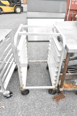 Metal bun/sheet pan rack on commercial casters, holds multiple pans, visible rust, sturdy condition, ideal for bakeries.