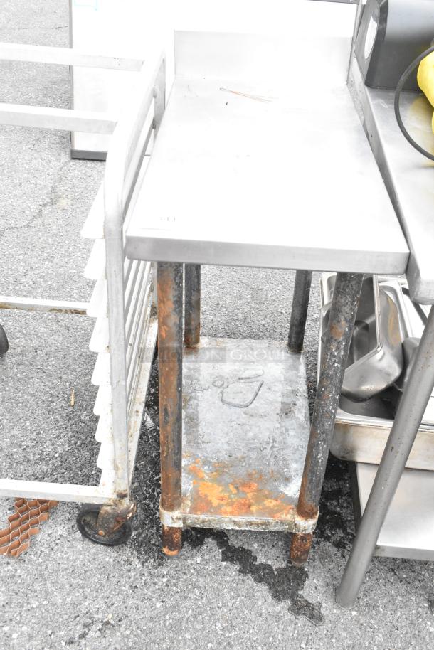 Stainless steel table with metal under shelf, featuring a back splash. Some rust and wear visible on legs and shelf.