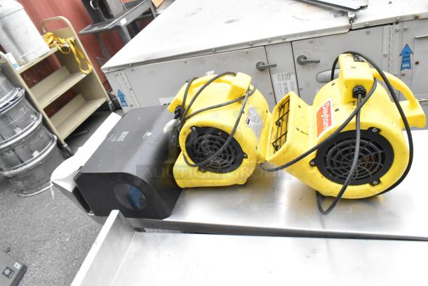 Stainless steel table with metal under shelf and back splash, includes two yellow Dayton air mover fans, used condition.