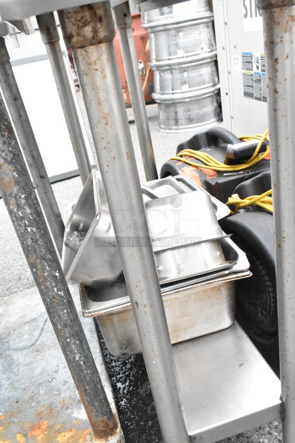 Stainless steel table with metal under shelf and back splash. Includes two Dayton air mover fans. Visible rust and wear.