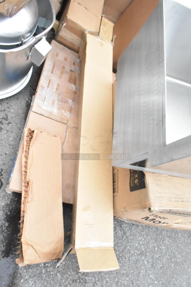 Boxes with new scratch and dent items including salad bowls, concrete level, and mop sink; items display some packaging wear.