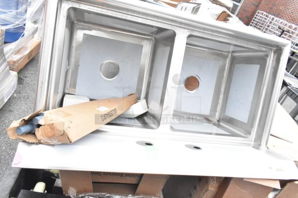 New dual-compartment stainless steel sink with visible scratches and dents, includes a partially damaged box containing installation parts.