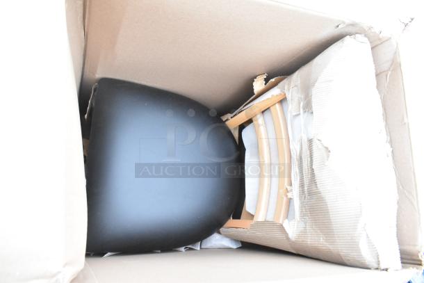 Cardboard box containing new, scratch and dent items including a black seat and wooden components, showing minimal wear.