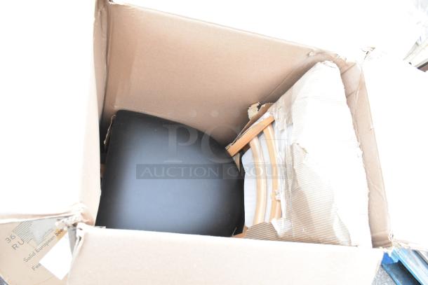 Cardboard box with assorted new scratch and dent items, including a black seat, wooden chair legs, and packaging material.