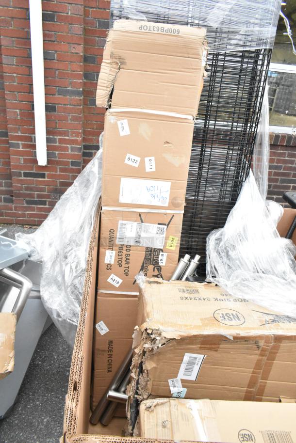 Cardboard boxes with scratch and dent wire shelves, sink, and drawer, wrapped in plastic. Item tags are visible.