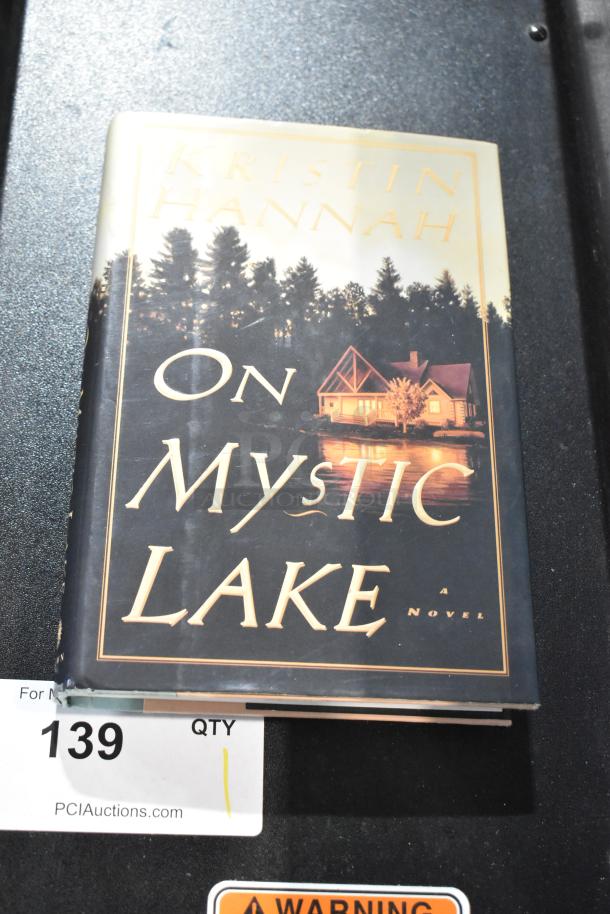 Hardcover book "On Mystic Lake" by Kristin Hannah. Features serene lake house cover art. Book in good condition.