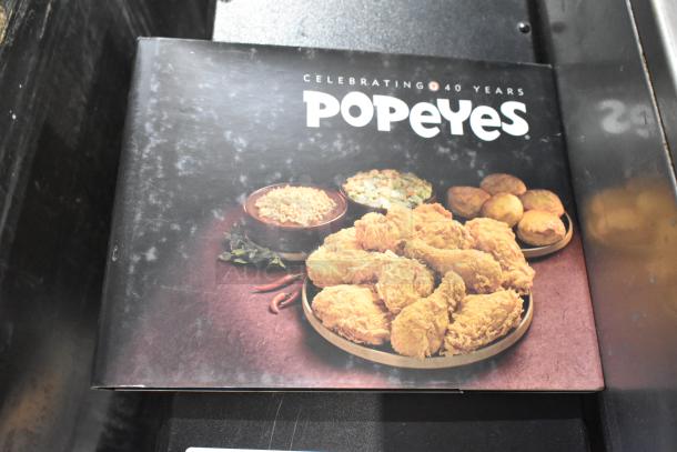 Popeyes 40th Anniversary book cover featuring fried chicken, rice, and biscuits on a black background.
