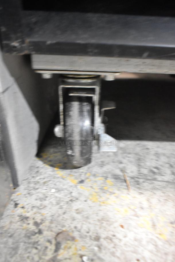 Commercial caster wheel of Avantco 178GDC12FHCB reach-in cooler, metal frame, slight wear visible. Ideal for maneuverability.