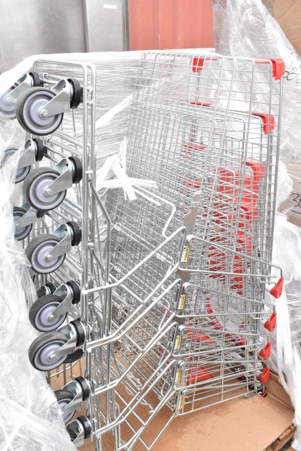 Four brand new chrome finish shopping carts with minor scratches and dents, stacked and wrapped, with red handles and swivel wheels.