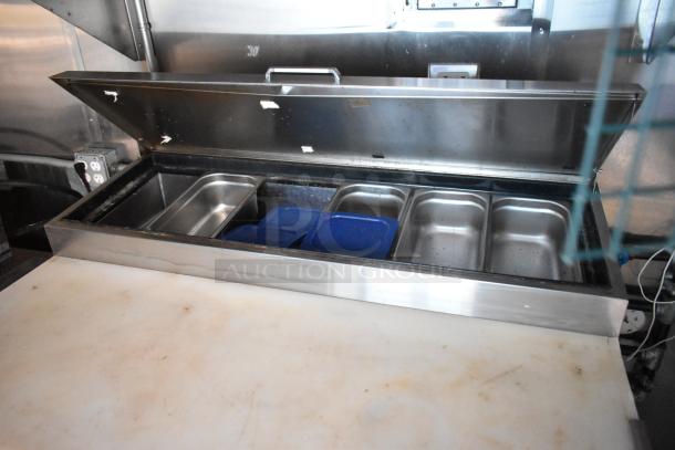 Open commercial-grade food prep table with stainless steel compartments, visible in mobile kitchen trailer.